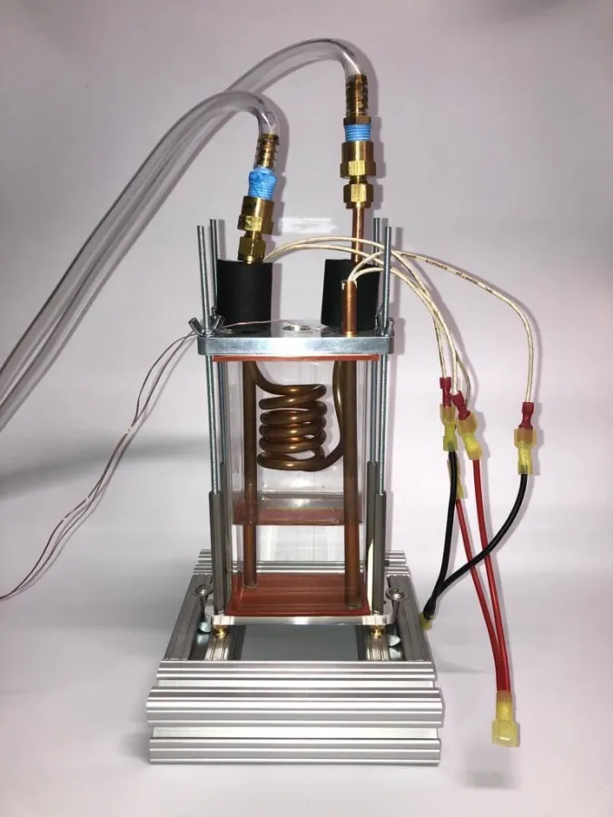 The heat transfer chamber: a glass tube between aluminium plates, containing a copper condensing coil and two copper rods housing cartridge heaters, with thermocouple and power leads attached.