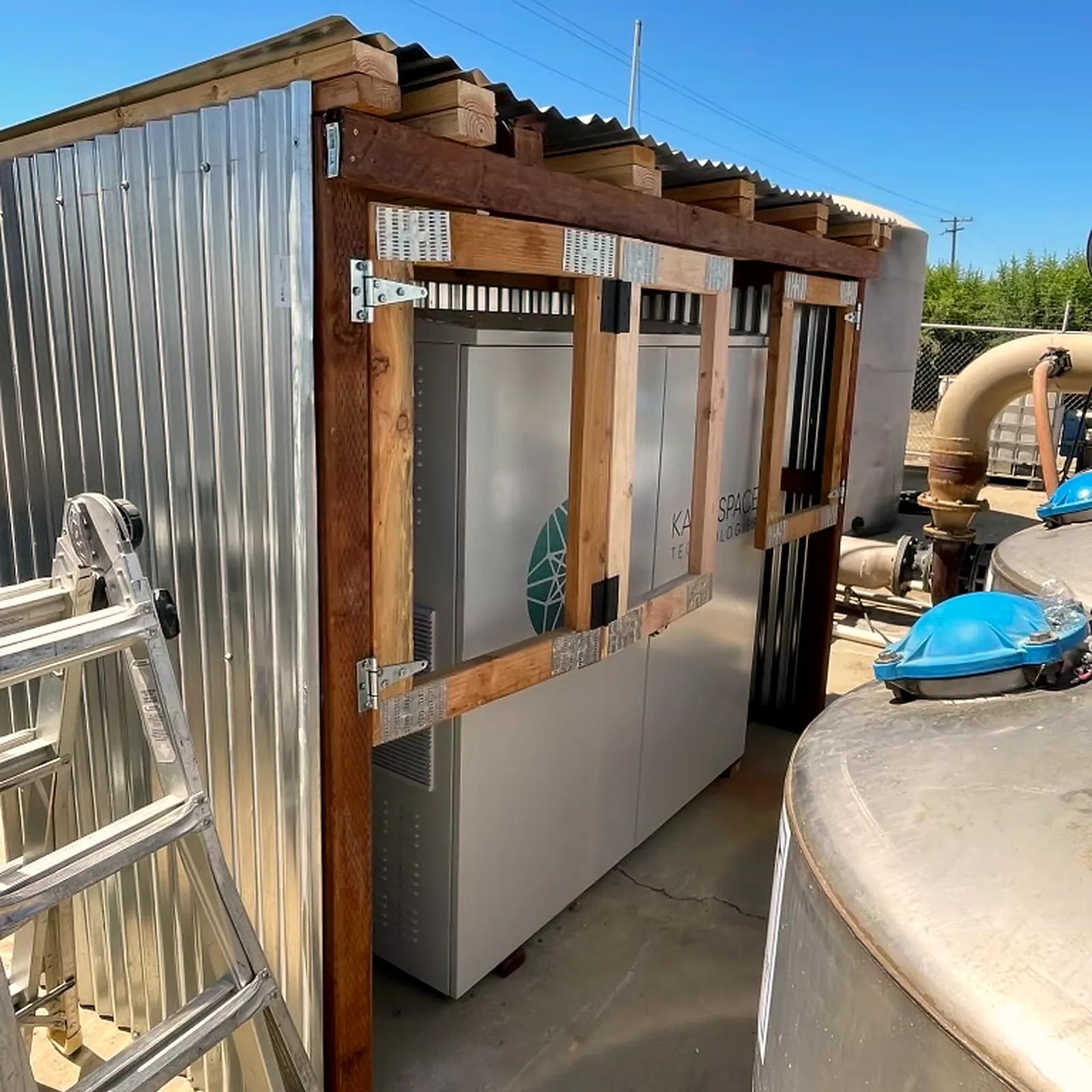 Oxygen concentrator cabinets under a corrugated shelter beside stainless water tanks
